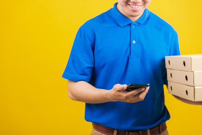 Midsection of man using mobile phone against yellow background