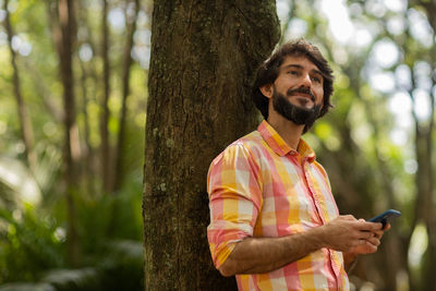 Young man with smartphone at day time with a green park in the background. mobile phone, technology,