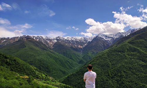 Rear view of man looking at mountains against sky