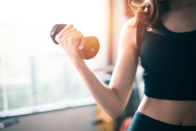 Midsection of woman lifting dumbbell at gym