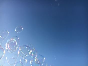 Low angle view of bubbles against clear blue sky