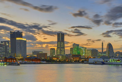 River by modern buildings against sky during sunset