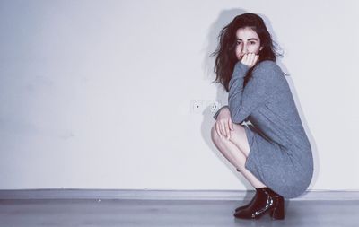 Side view portrait of young woman crouching against white wall