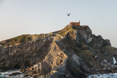 Paving stone way leading along stone bridge and ridge of rocky hill to lonely country house on island gaztelugatxe surrounded by tranquil sea water with white foam waves