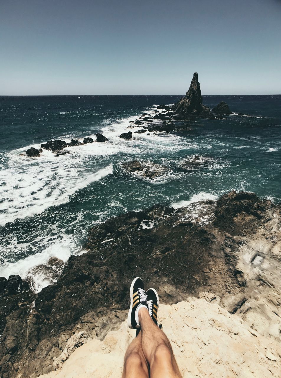 sea, water, beach, land, horizon, sky, personal perspective, horizon over water, low section, human body part, scenics - nature, nature, human leg, one person, beauty in nature, body part, clear sky, rock, day, outdoors, human foot