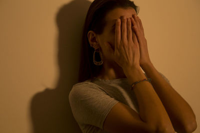 Woman covering face with hands against wall