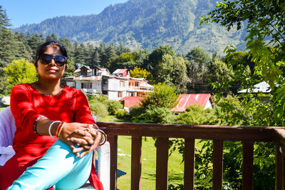 Woman wearing sunglasses sitting against railing and trees