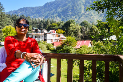 Young woman with sunglasses on railing against trees