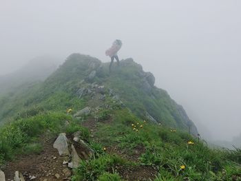 Man standing on rock against sky during foggy weather
