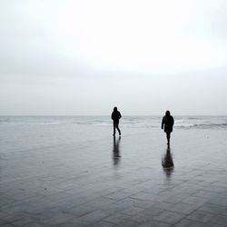 Silhouette man and woman walking on promenade against sky