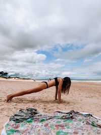 Rear view of woman sitting on sand at beach against sky