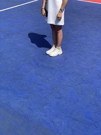 Low section of woman standing on blue umbrella