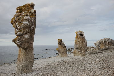 Rock formations at beach against cloudy sky