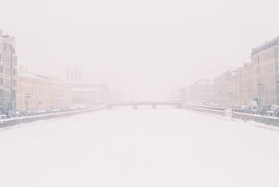 Snow covered road by buildings in city against sky