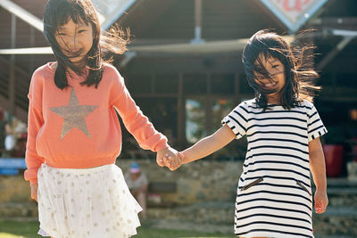 Portrait of smiling sisters holding hands against house