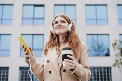 Young woman using smart phone while standing against buildings