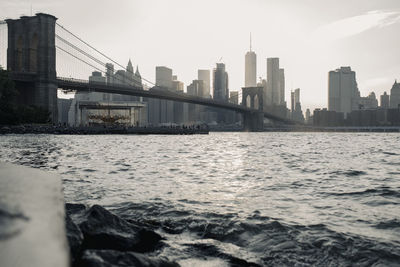 Amazing low angle cityscape of new york city with brooklyn bridge over river and skyscrapers in sunlight at sunset time