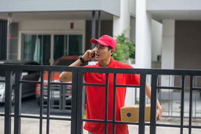 Delivery man standing at closed gate against buildings