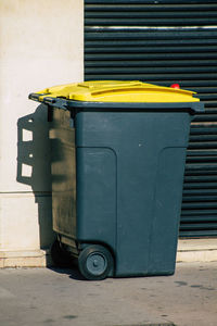 Garbage bin on sidewalk against wall in city