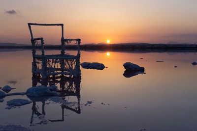 Wooden posts in lake against sky during sunset