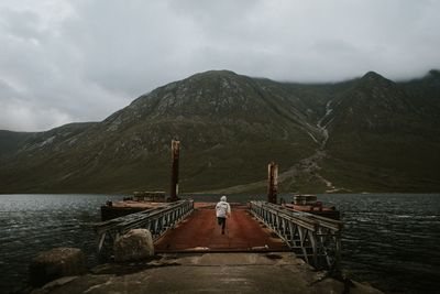 Rear view of man standing on pier over lake against mountains