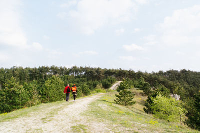 Rear view of two people walking on dirt road