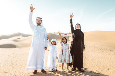 Happy family showing peace sign while standing on sand dune
