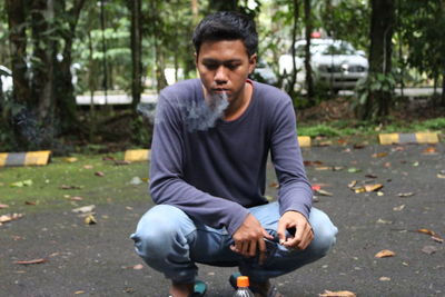 Young man crouching and smoking on street in city