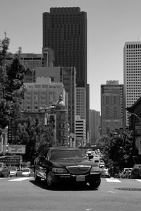 Cars on road by buildings in city against sky