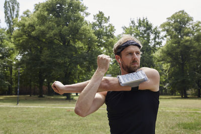 Man listening music while exercising against trees in park