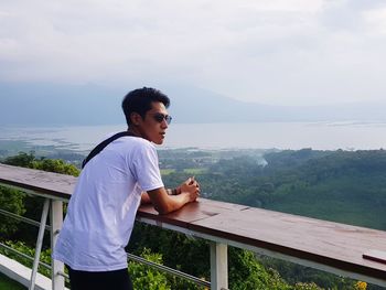 Side view of young man standing by railing against sea