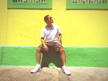 Full length of young man sitting against yellow wall