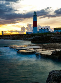 Lighthouse by sea against sky during sunset