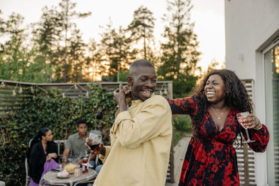 Happy woman dancing with young male friend while celebrating during dinner party