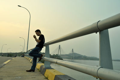 Side view of man standing on bridge against sky