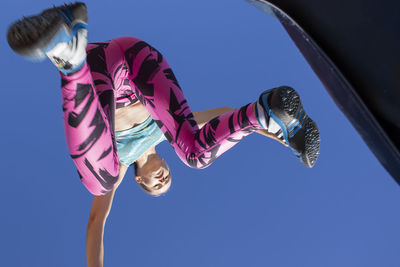 Low angle view of female athlete jumping against clear blue sky