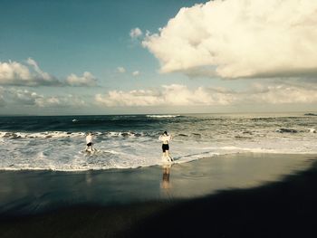 People at beach against cloudy sky