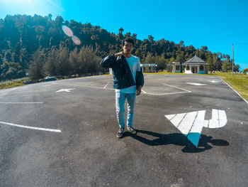 Portrait of young man standing on road during sunny day