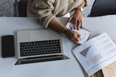 Businesswoman writing on diary while working on financial data at office