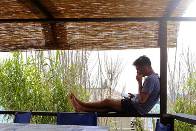 Side view of man sitting on window