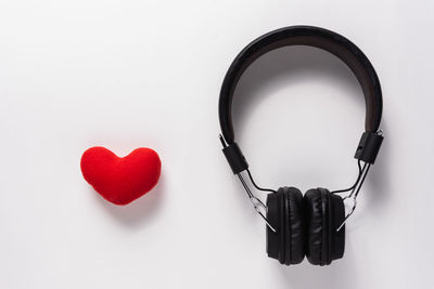 Close-up of red heart shape decoration by headphones over white background