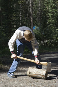 Man cutting wooden log while standing on road