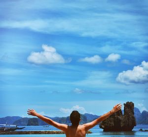 Rear view of woman with arms raised against sky