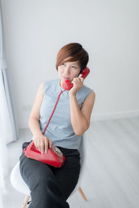 Woman using rotary phone while sitting on chair by window at home