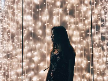 Side view of woman standing against illuminated lights at night