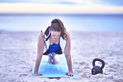 Young woman with arms raised on beach against sky