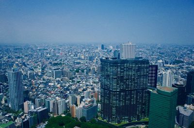 Aerial view of buildings in city against blue sky