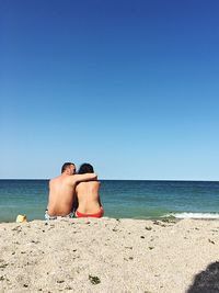 Rear view of shirtless man on beach against clear sky