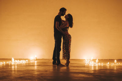 Man and woman standing on illuminated lamp against orange sky