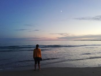 Rear view of man walking at beach against sky during sunset